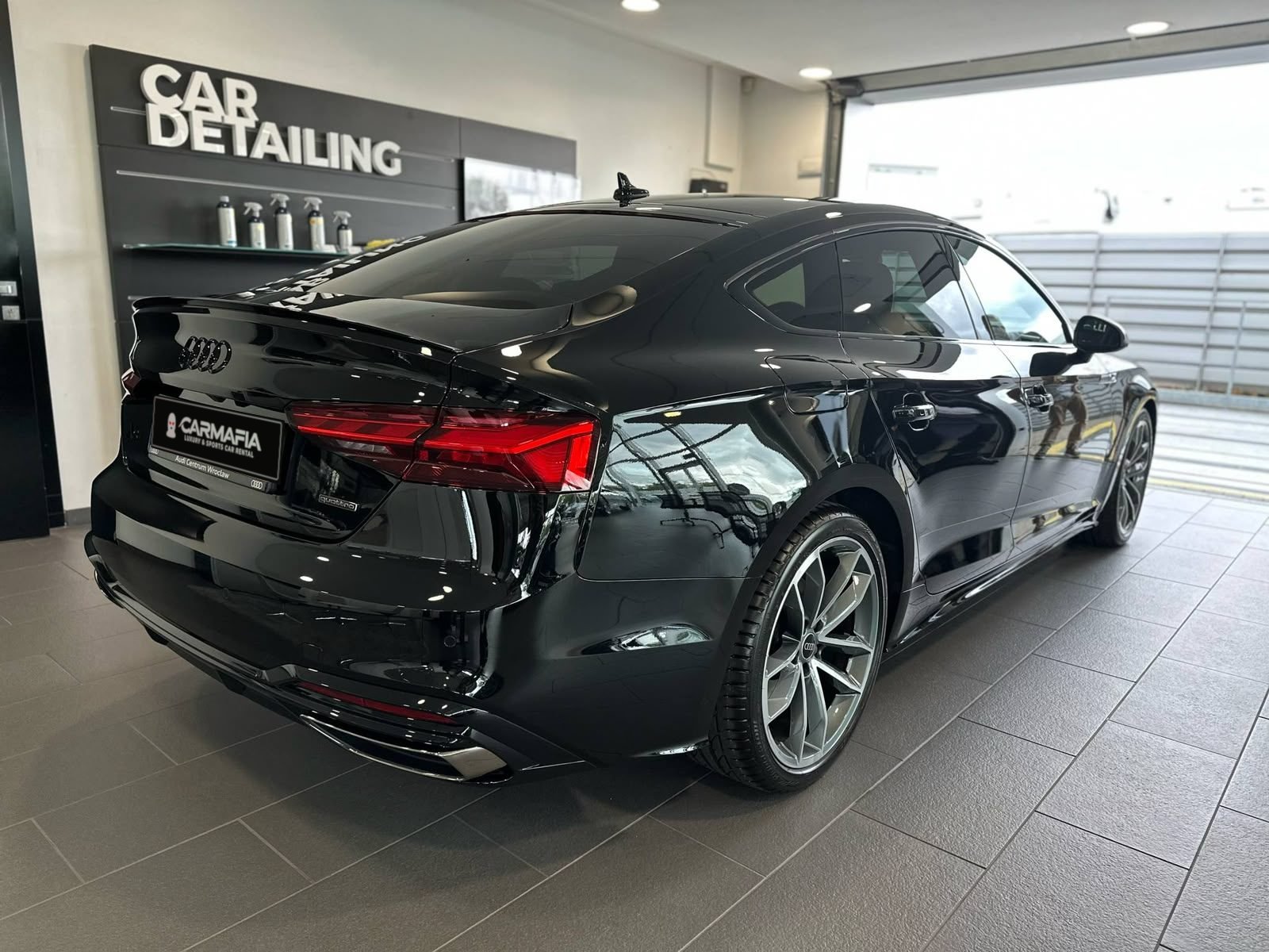 Tył czarnego Audi A5 Sportback w studiu detailingu, z tablicą CarMafia.fun